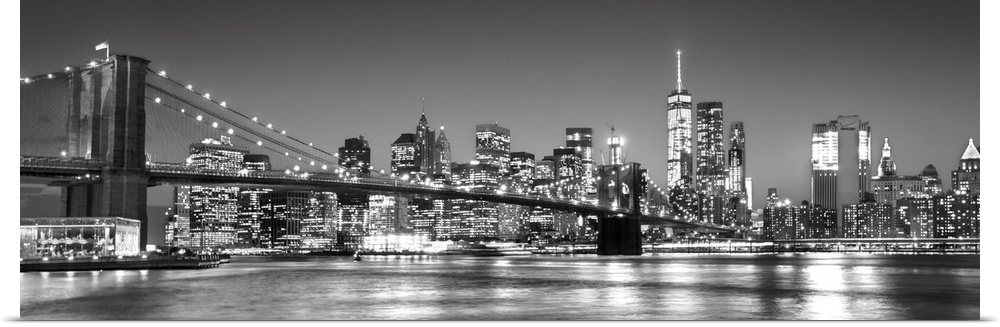 View of the New York City skyline illuminated at night, with the Brooklyn Bridge, from across the water.
