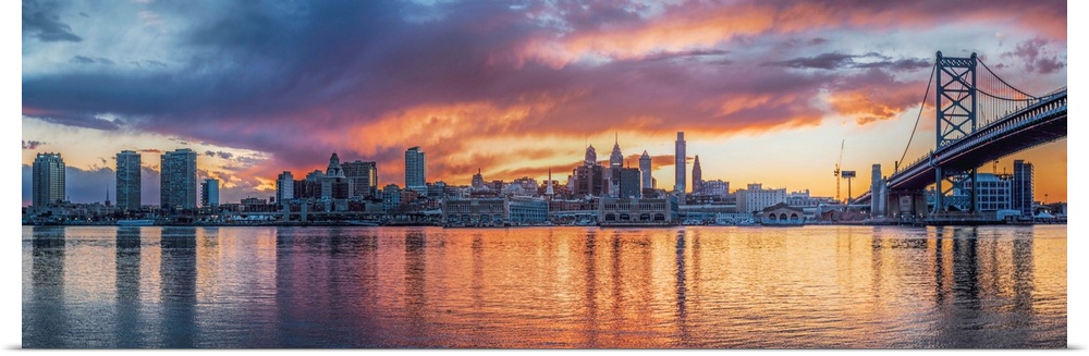 Panoramic view of a fiery sunset over the Philadelphia city skyline, with the Benjamin Franklin Bridge on the right.