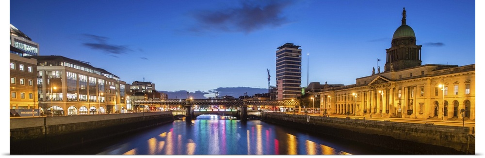 Panoramic photograph going straight down the River Liffey with buildings, highlighting The Custom House, on the sides lit ...