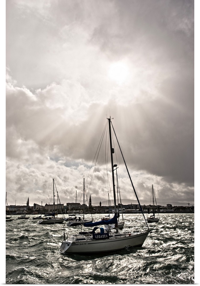 Photograph of the sun peaking through the clouds over the River Liffey in Ireland, and sailboats anchored around.