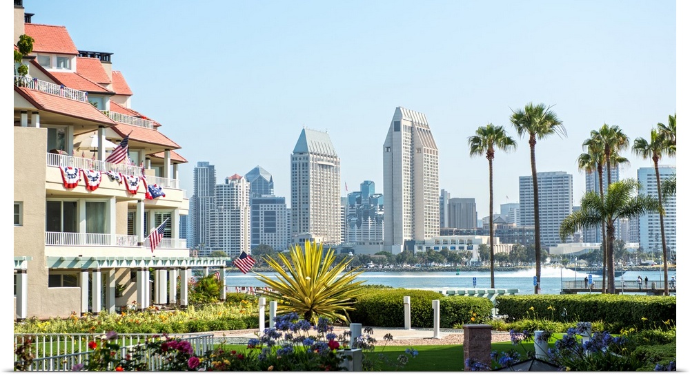 Photograph of part of the San Diego, California skyline with flowers, palm trees, and American flags in the foreground.