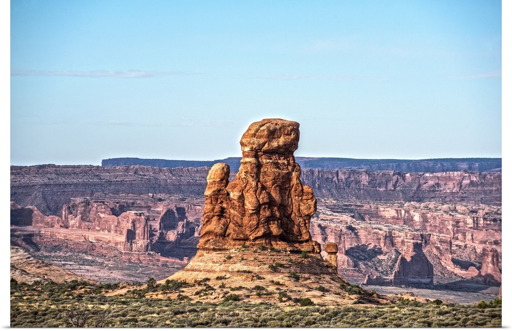 Sandstone tower overlooking the canyon and desert under a pale blue sky in Arches National Park, Utah