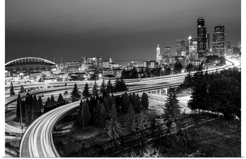 Panoramic photograph of the Seattle skyline at night with light trails from the car lights on the highway.