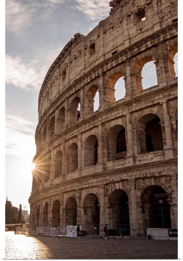 Photograph of the sun shining on the side of the Colosseum in Rome on a beautiful day.