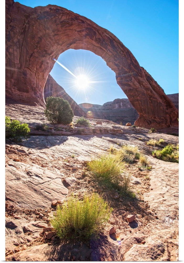 The sun framed by the Corona Arch under a blue sky in Arches National Park, Utah.