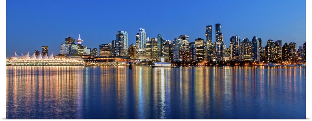Photograph of the downtown Vancouver skyline lit up at dusk and reflecting onto the water creating bands of color, Vancouv...