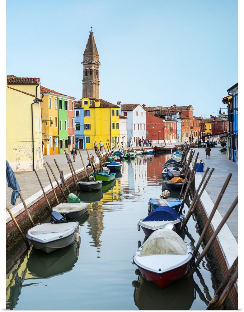 Photograph of docked gondolas in a small canal in the Venetian Lagoon in Burano, Venice, Italy with the Leaning Bell Tower...