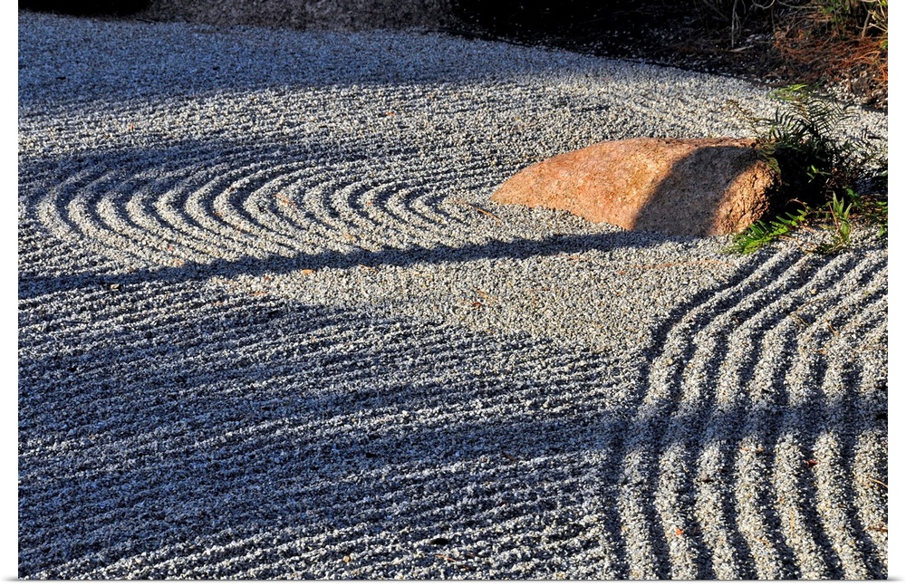 An embedded rock catches the afternoon sun in a raked rock garden.