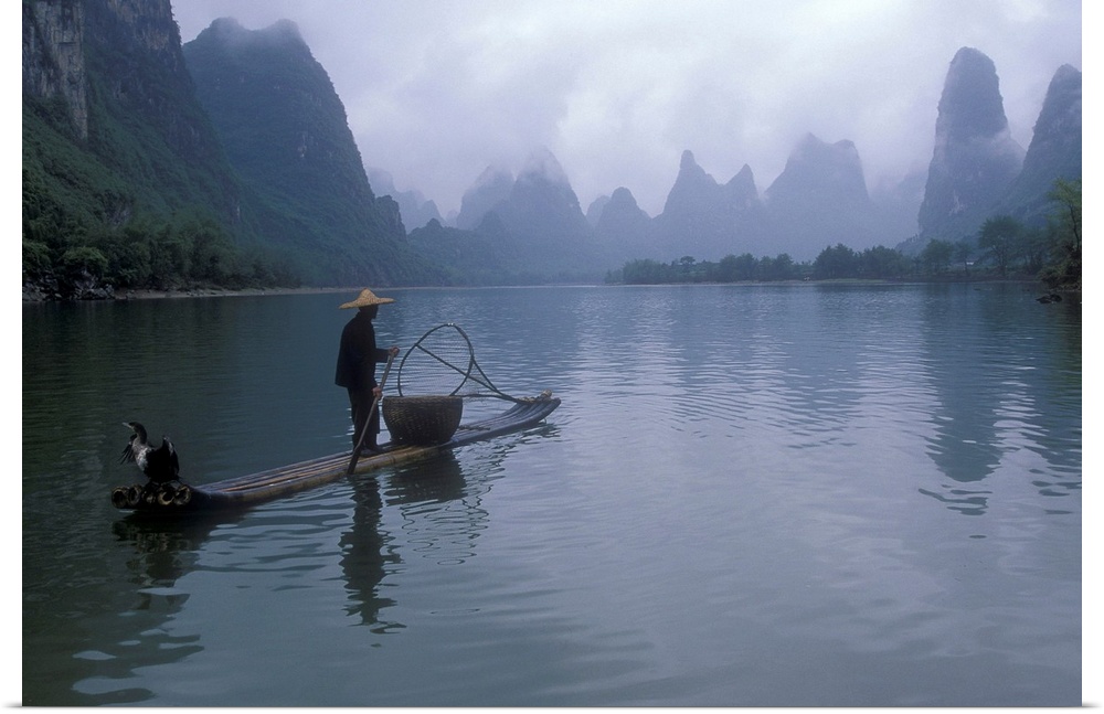A fisherman is photographed paddling his raft toward immense cliffs that are shown through a layer of fog.