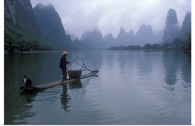 Cormorant fisherman poles a bamboo raft near limestone karst mountains, Li River, People's Republic of China