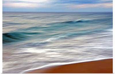 Teal and white surf flows on a rust-colored beach under blue clouds