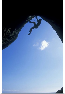 A climber ascending a cave archway at Foxhole, Gower Peninsula, Wales, UK