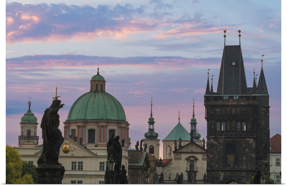 Details of statues and spires at Charles Bridge at sunrise, featuring dome of Church of Saint Francis of Assisi and Old To...