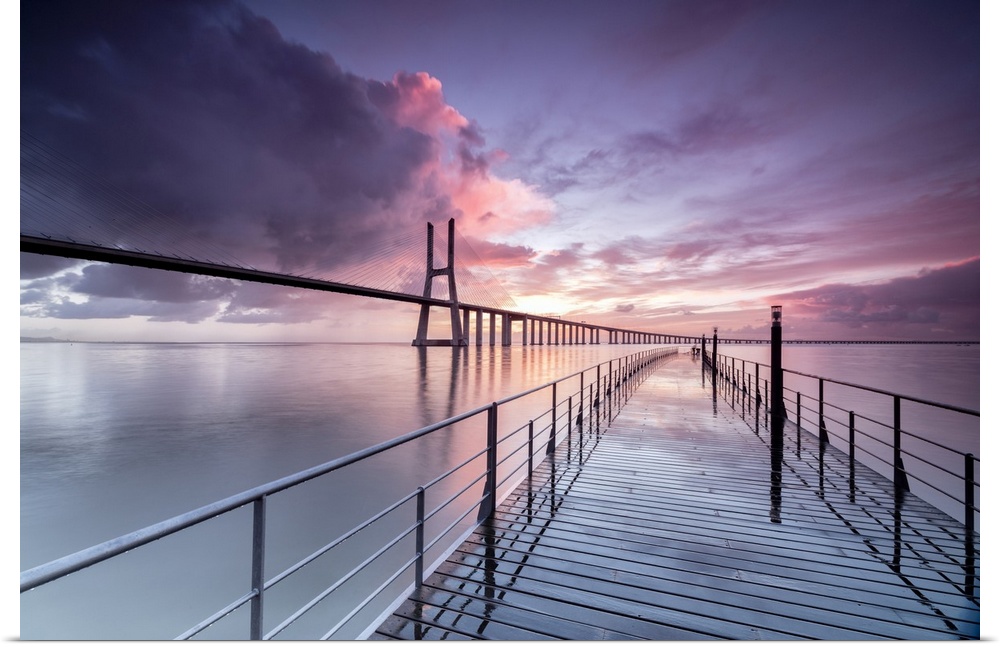 Sunrise colors the clouds reflected in Tagus River and frame the Vasco da Gama bridge in Lisbon, Portugal, Europe