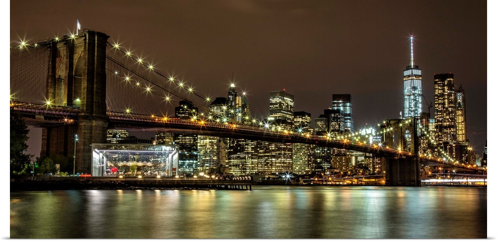 Panoramic photograph of the Brooklyn Bridge illuminated at night, reflected in the water below, with the New York City sky...
