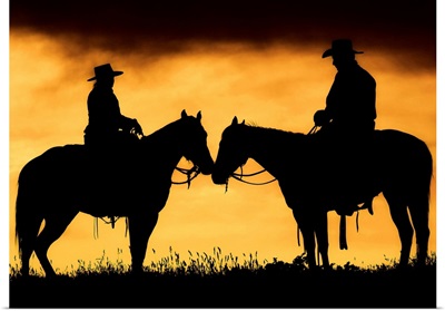 Cowboy and cowgirl on horseback in silhouette at sunset