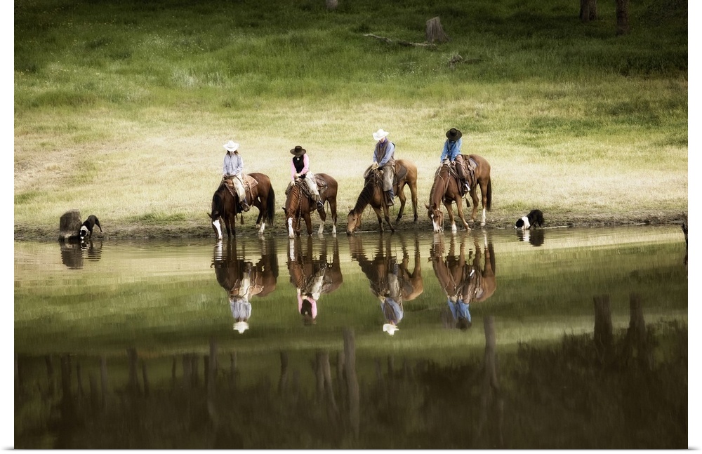 Photograph of horseback riders and their dogs by water at dusk.  The riders and horses and reflected in the water.