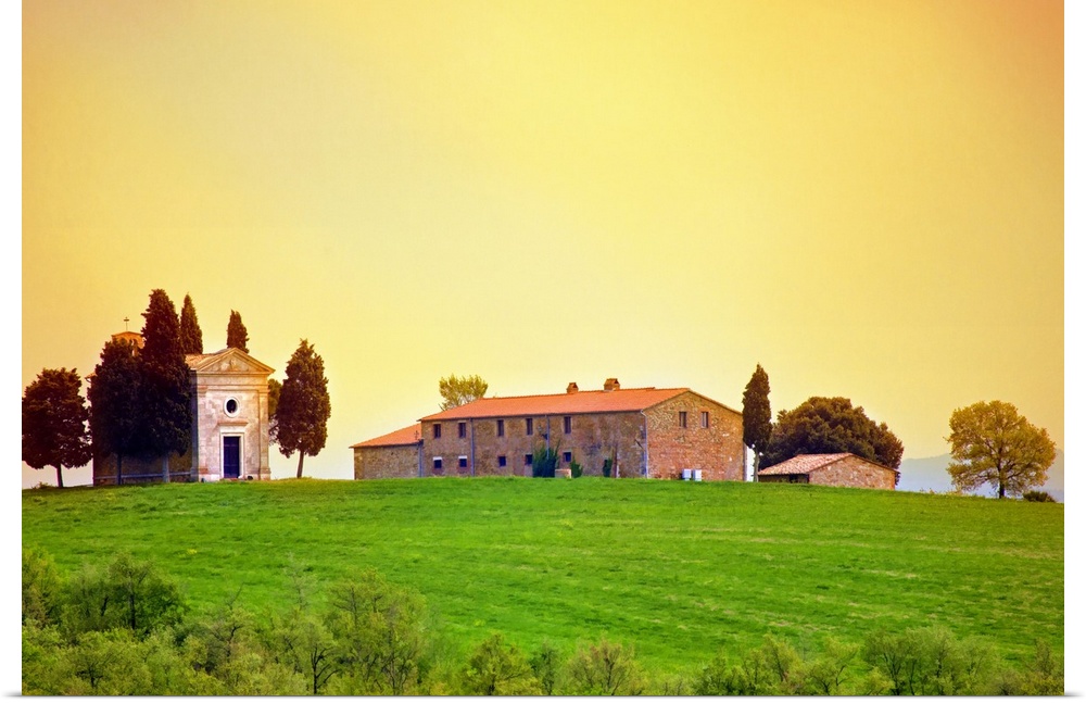 Old traditional Tuscan farm buildings set on a green grass hill with a clear sunset sky.