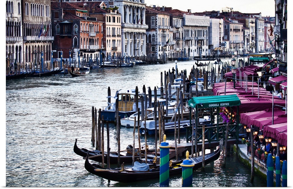 Gondola boats sit in the water which curves toward the back of the picture and is lined on either side by buildings and do...