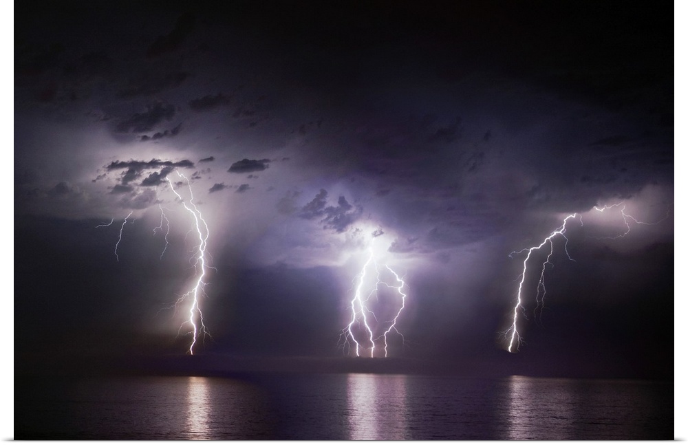 Time-lapse photo of three bolts of lightning striking the ocean from storm clouds at night, illuminating the dark sea.