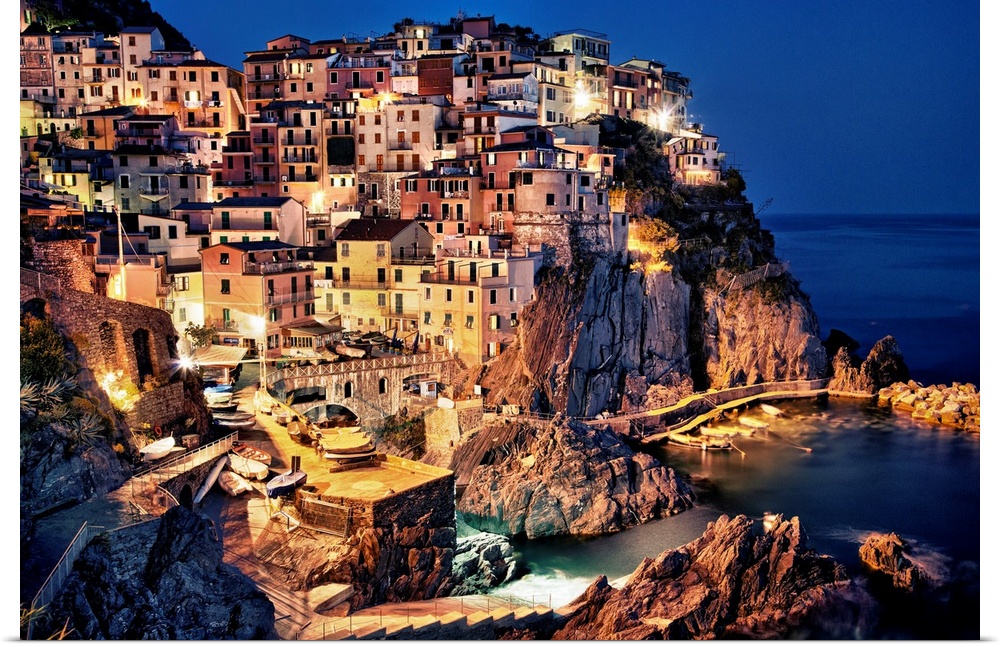 Large photograph taken of homes and buildings sitting within the rocky cliffs of a city in Europe at night.  The bright li...