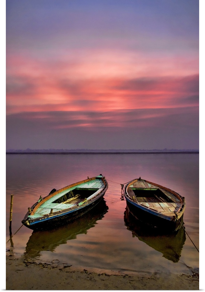 Picture of two empty wooden boats tied to the sandy shore in the early morning sunrise.