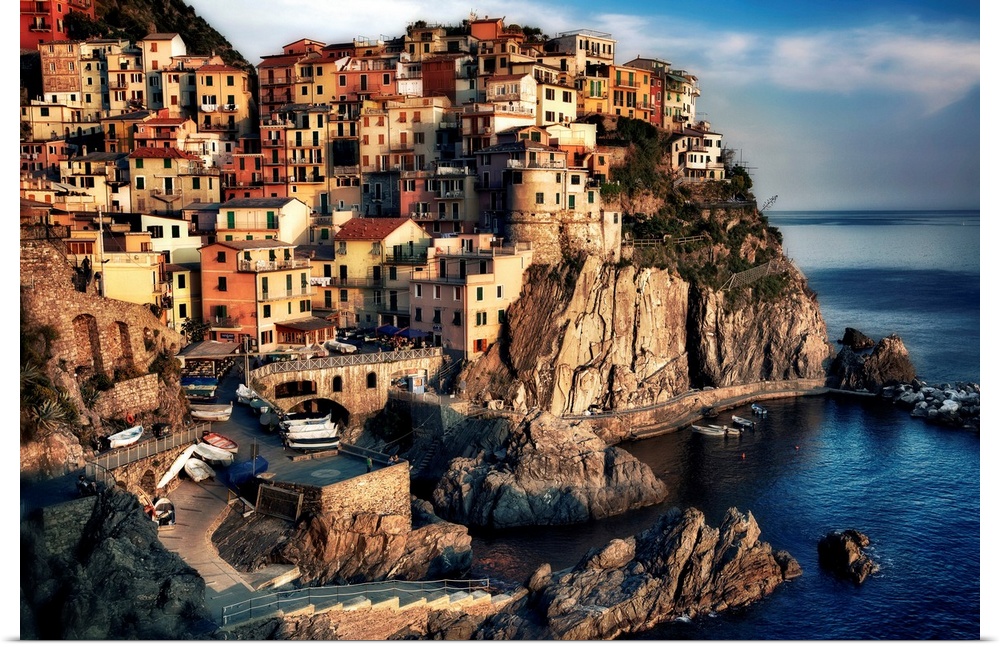 A small town sits in and on a cliff right near the water. The sun has begin to set shining brightly onto the houses.