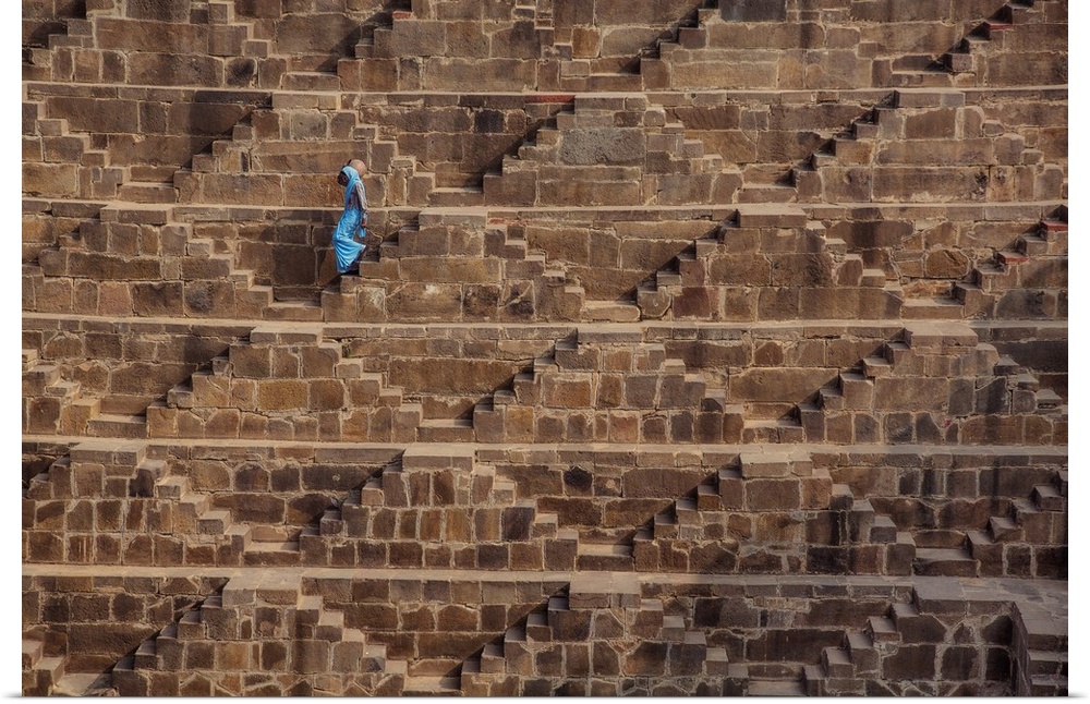 Woman with blue Sari walking to get water in the Chand Baori Step Well in India.