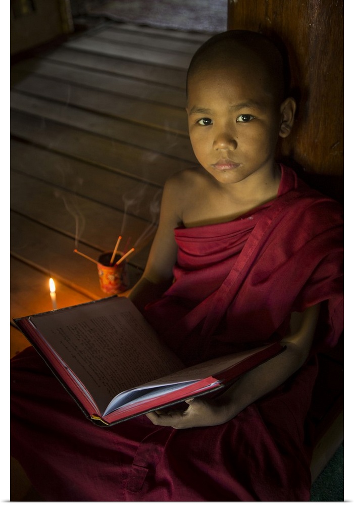 Young Burmese monk reading by candlelight