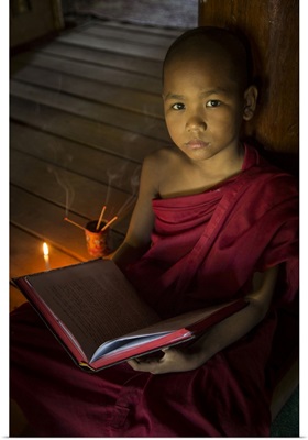 Young Burmese monk reading by candlelight