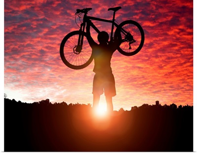 Silhouette Of a mountain biker holding up bike against a sunset sky