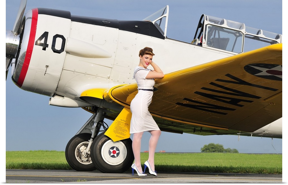 1940's style Navy pin-up girl leaning on the wing of a T-6 Texan trainer aircraft.