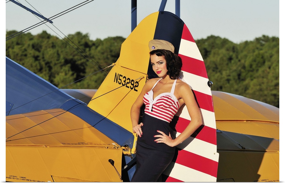 Patriotic 1940's style pin-up girl leaning on the tail fin of a World War II Stearman biplane.