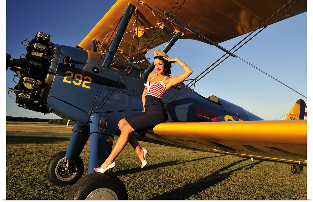 Patriotic 1940's style pin-up girl sitting on the wing of a World War II Stearman biplane.