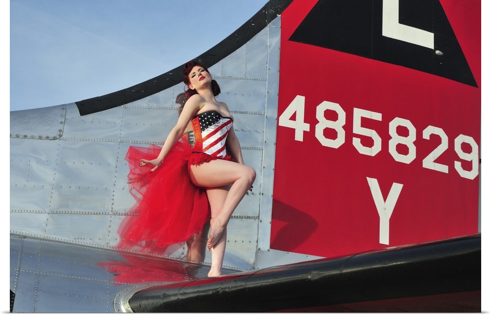 Beautiful 1940's style pin-up girl standing on the tail of a B-17 bomber.