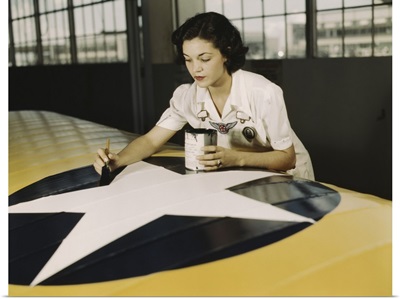A civil service worker paints the American insignia on a repaired Navy plane wing