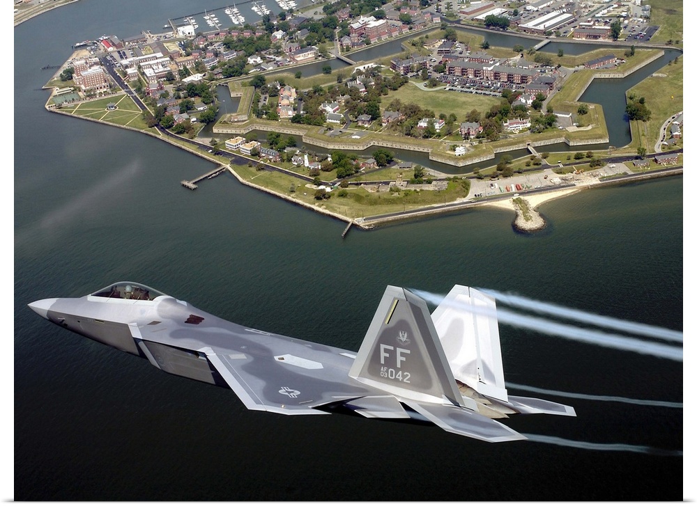 A militarty fighter jet flies past Fort Monroe with water vapor trails shooting from the wings of the plane.