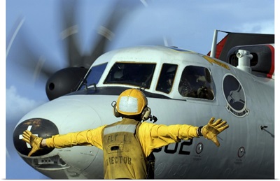 A flight deck director signals the pilot of an E-2C Hawkeye to spread his wings
