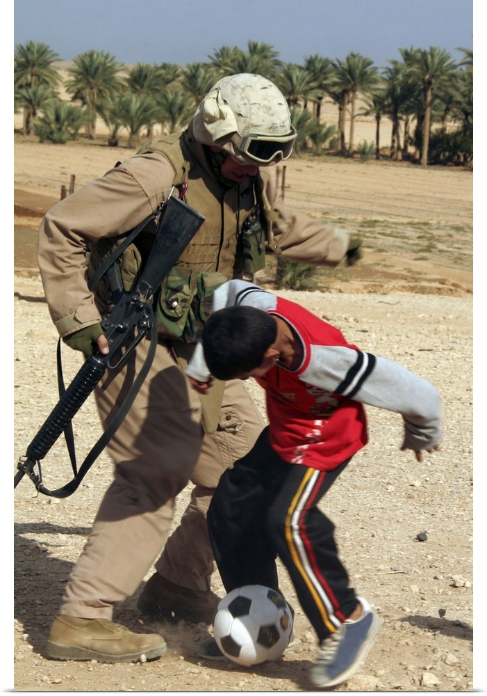 A soldier plays soccer with an Iraqi boy.