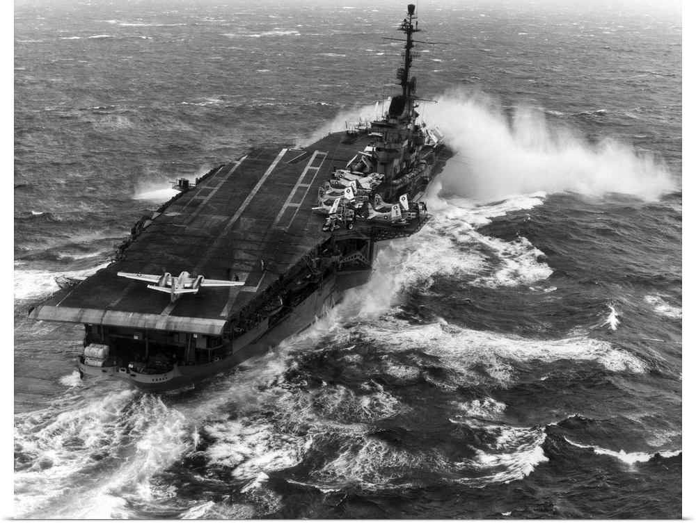 Aircraft carrier USS Essex (CVA-9) taking spray over the bow while steaming in heavy seas.
