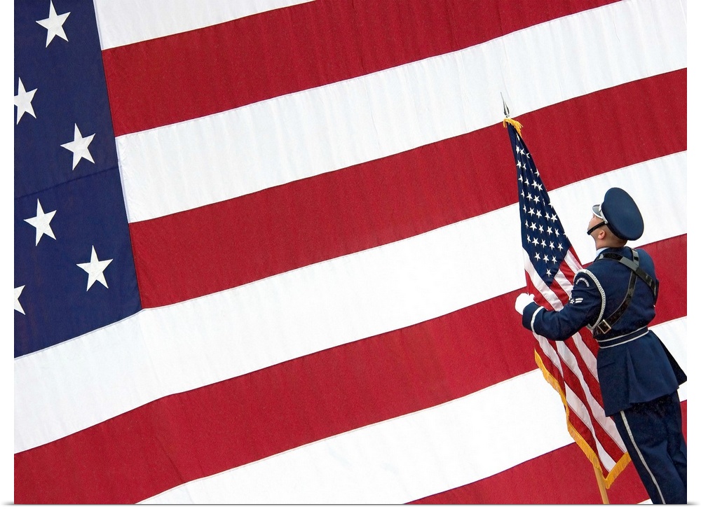 A soldier stands in front of a massive American flag while holding a smaller flag during the change of command ceremony.