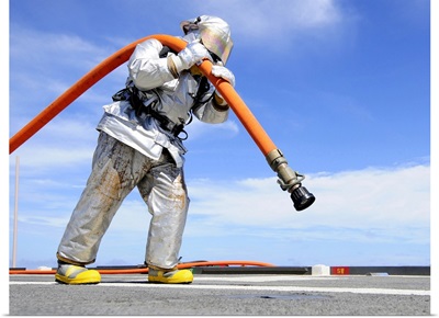 Firefighter Carries A Charged Hose Across The Flight Deck Of USS Denver