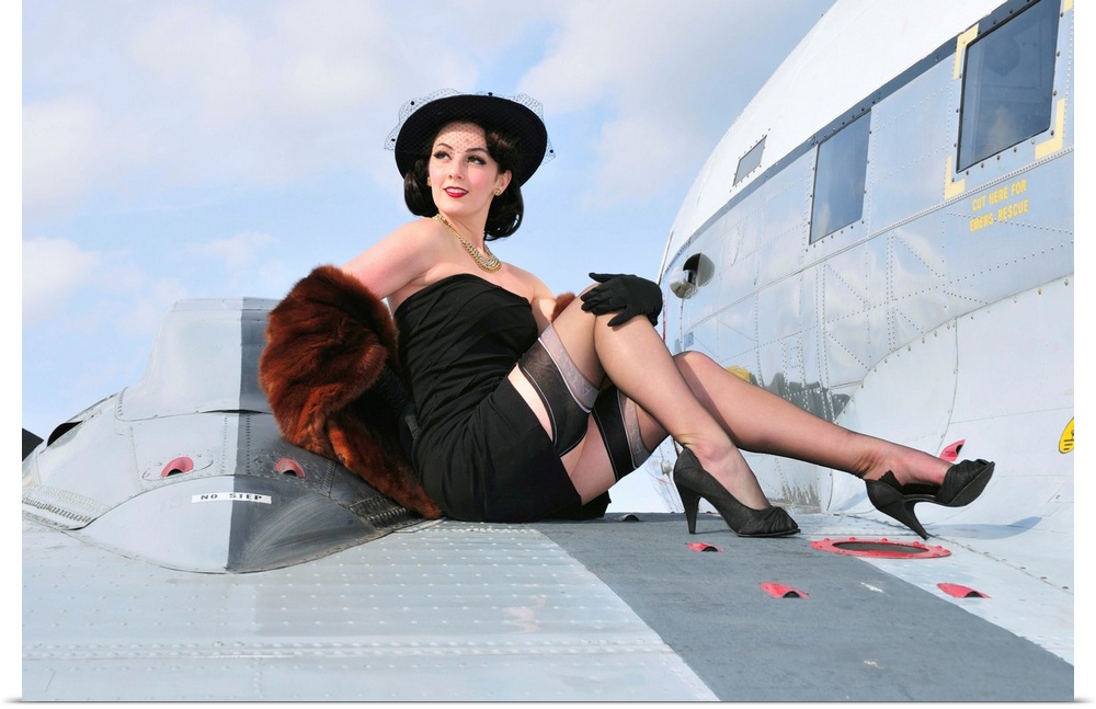 Glamorous woman in 1940's style attire sitting on a vintage aircraft.