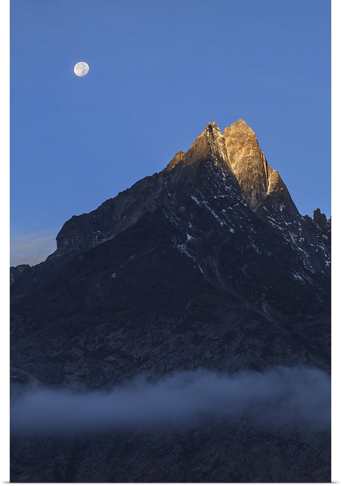 Moonset and alpenglow over a snow peak in the Himalayas as seen from Sagarmatha National Park of Nepal.