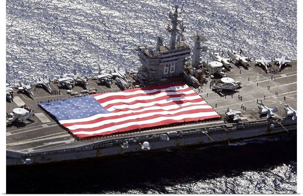 Canvas print of a big American flag being held next to planes sitting on top of a huge navy ship.