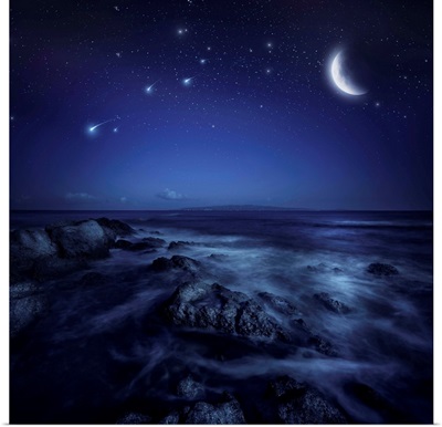 Rising moon over ocean and boulders against starry sky