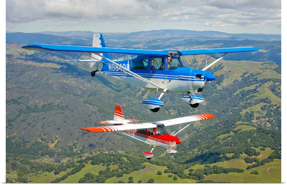 Two small airplanes are photographed while in flight over vast open land.