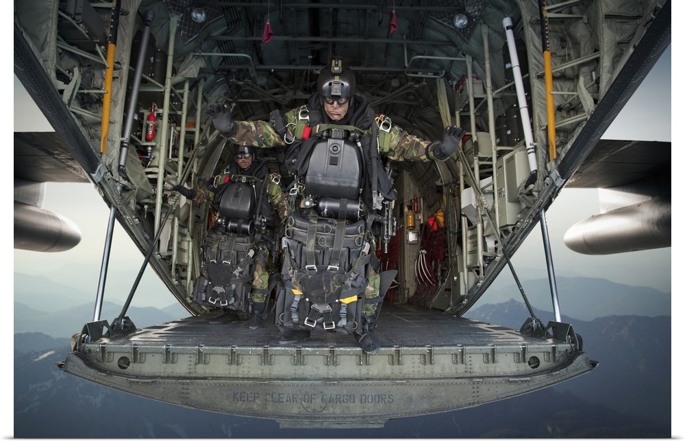 Landscape photograph of a U.S. Navy SEAL combat diver, loaded with gear, preparing to jump from the back of a C-130 Hercul...