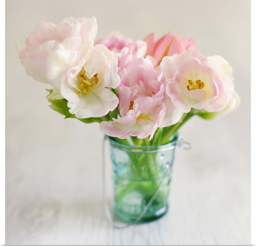 Square photograph of arranged pink and white flowers in a blue toned mason jar on a wooden table.