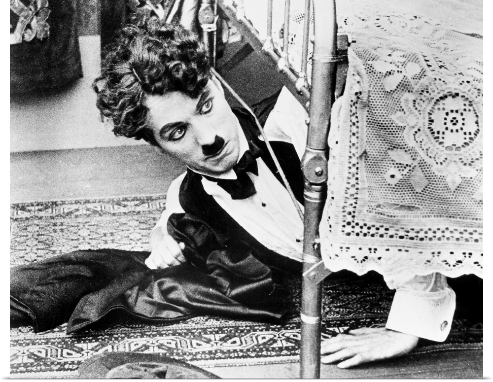 Charles Spencer Chaplin. English comedian. Getting out from under the bed in one of his silent movies from the 1920s.